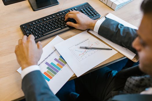 Business professional reviewing charts at desk, analyzing financial trends.